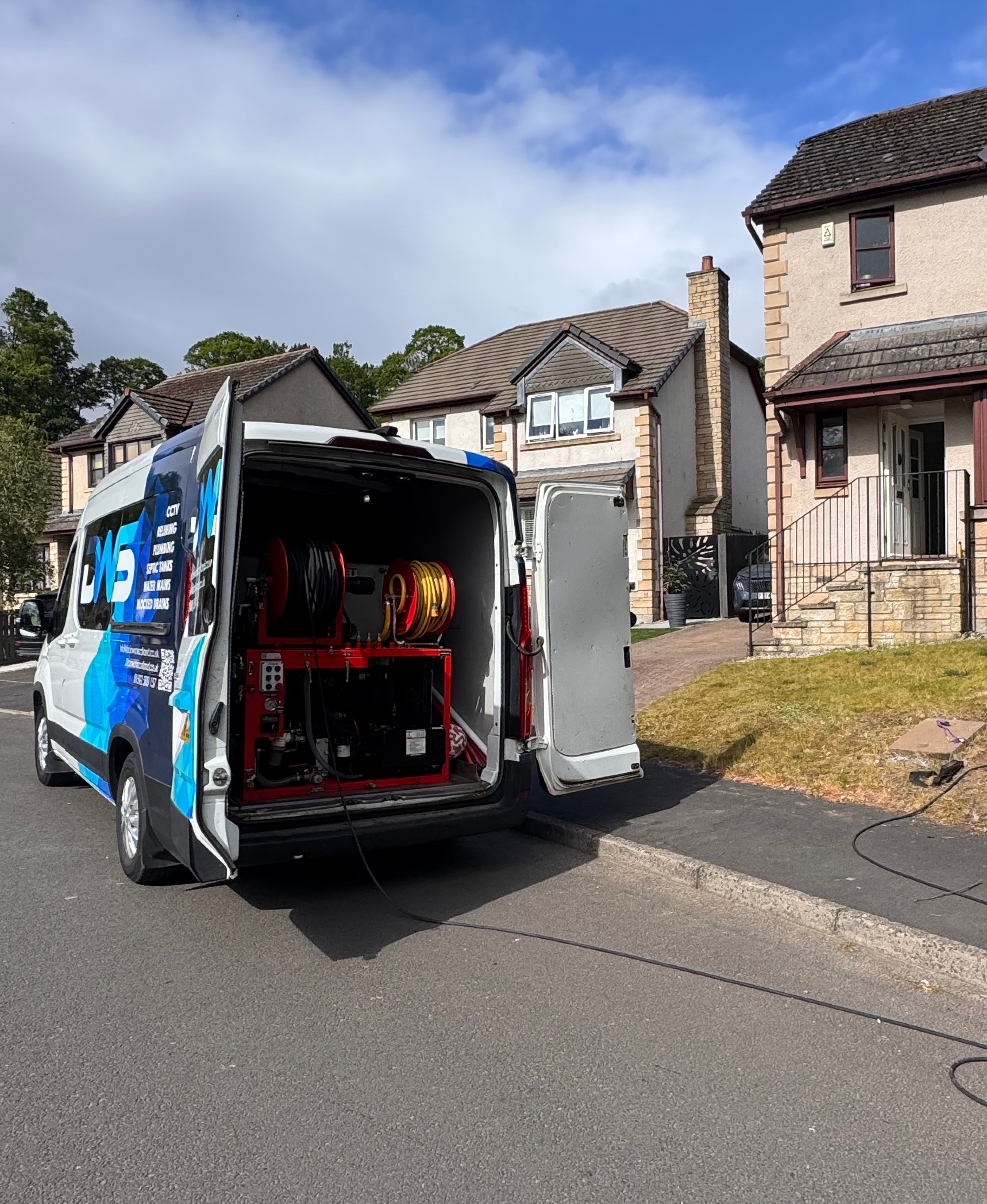 Drainage engineer operating high-pressure drain jetting equipment beside a home
